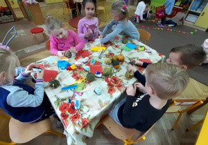 Dzieci siedzą przy stoliku i przyklejaja ozdoby na dynie
